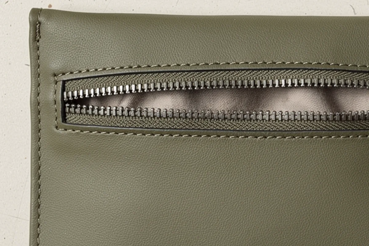 Close-up of an olive leather-like pouch showing its zipper opening and lining