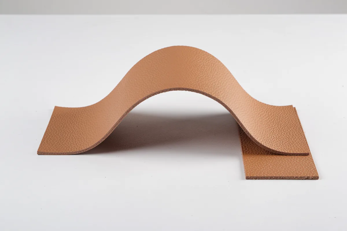 Tan coated material strip curved into a broad arch beside a flat swatch