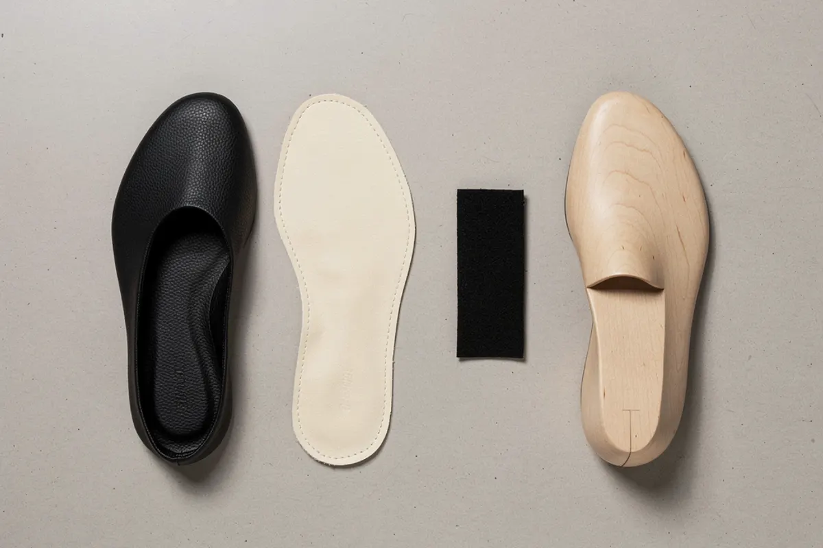 Black footwear shell, light insole, small dark swatch and wooden last arranged on a table